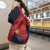 A person is holding a red and blue canvas fashion backpack in a brightly lit indoor space.