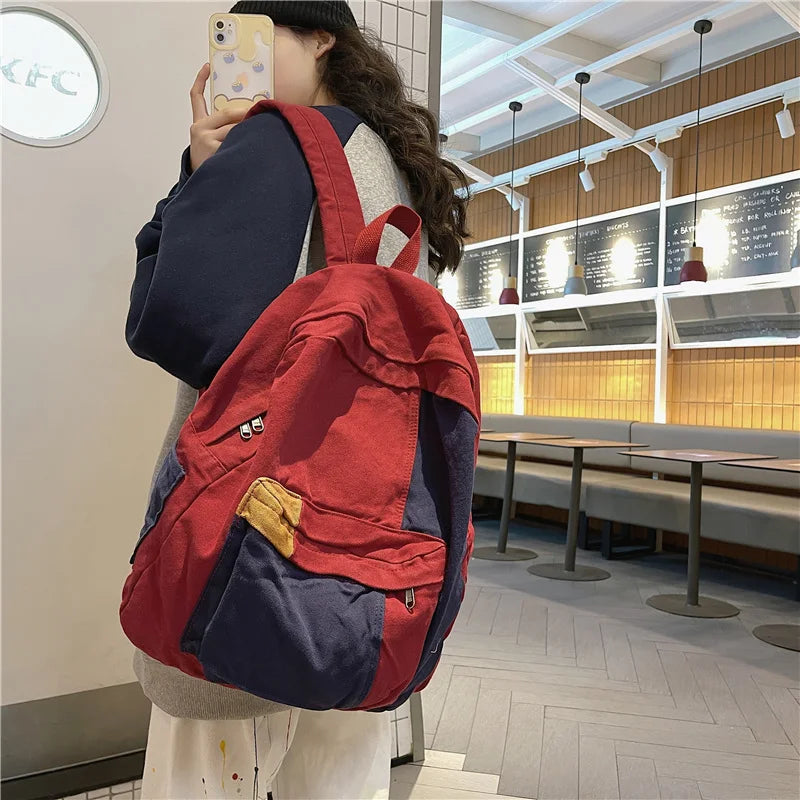 A person is holding a red and blue canvas fashion backpack in a brightly lit indoor space.