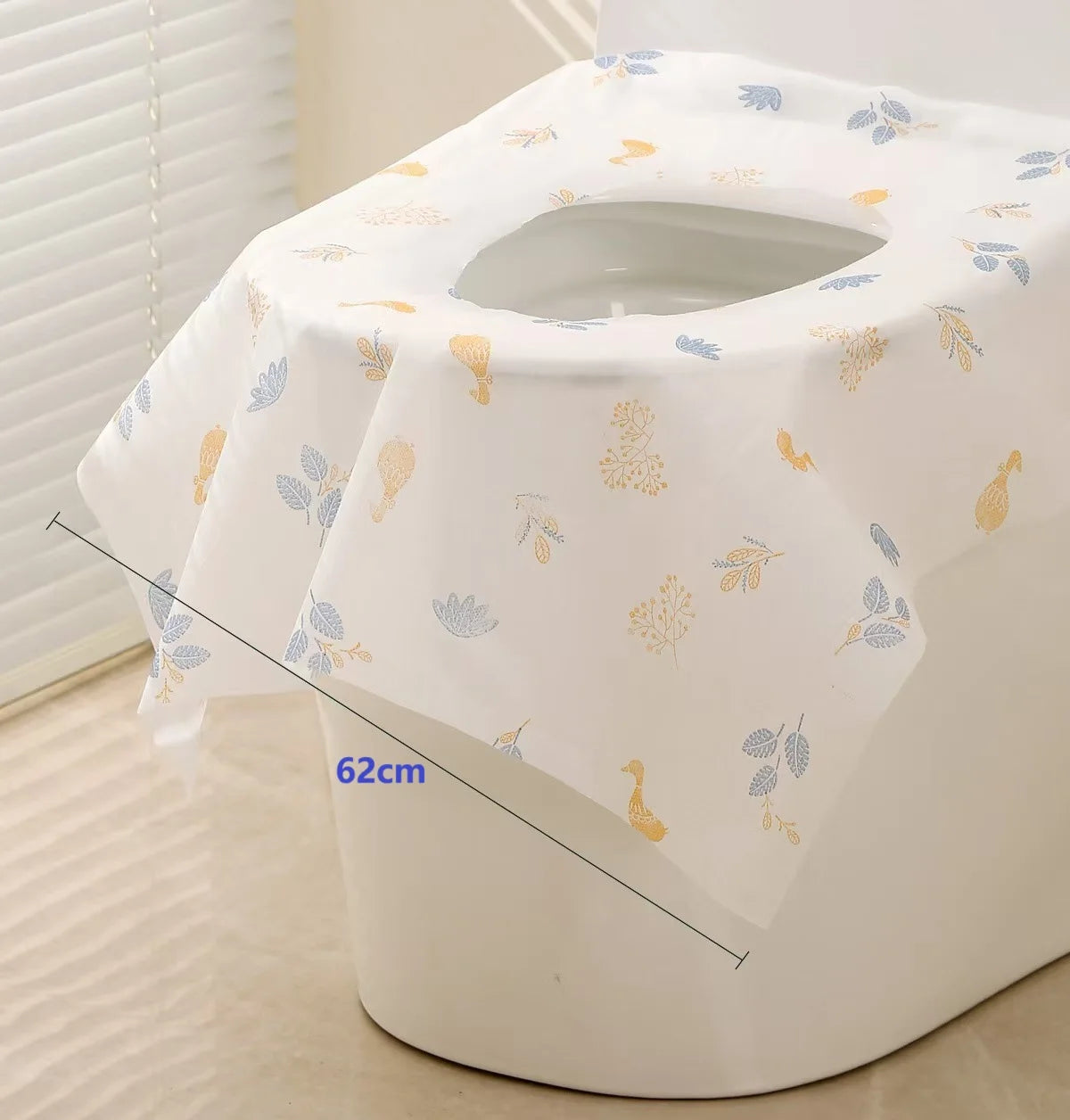 A white disposable toilet seat cover is shown rolled up, featuring gold and blue leaf patterns.