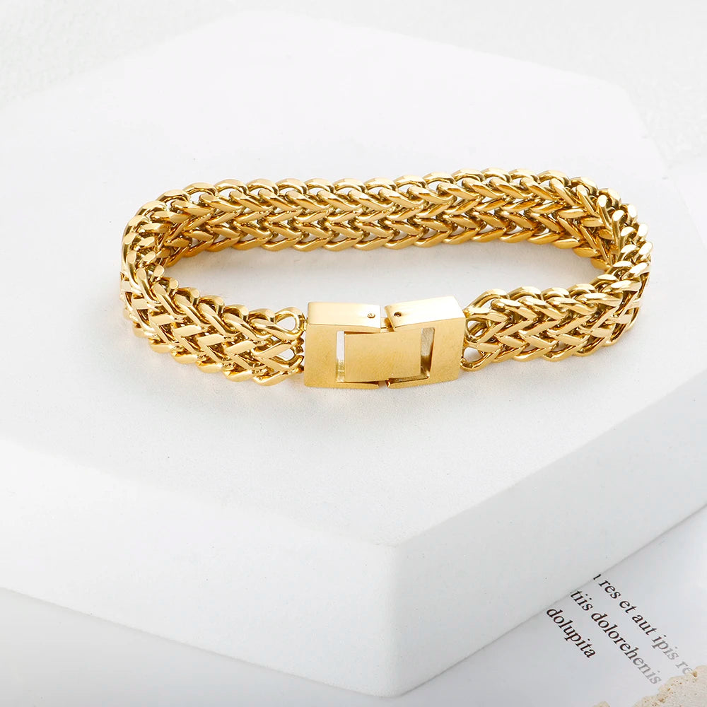 A chunky gold link chain bracelet worn on a white surface.