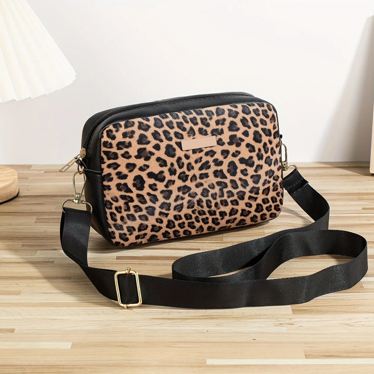 A black leopard print crossbody bag with a gold buckle strap resting on a wooden surface.