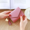 A hand holds a pink waterproof nylon crossbody bag with gold tassel and a heart charm on a wooden table.