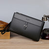A black men's PU leather clutch bag with silver hardware resting on a wooden surface.