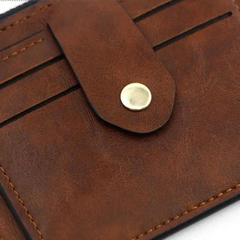 A close-up of a brown leather card holder wallet with stitching and a round brass stud closure.