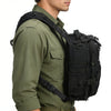 A person wearing a olive green shirt and black multi-compartment crossbody bag with tactical straps.