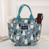 Bolsa térmica de color verde azulado con estampado, que tiene un asa y un diseño de gato blanco.
