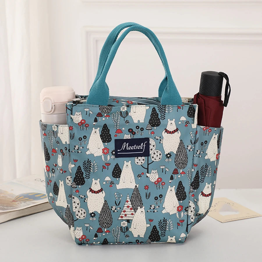 Bolsa térmica de color verde azulado con estampado, que tiene un asa y un diseño de gato blanco.