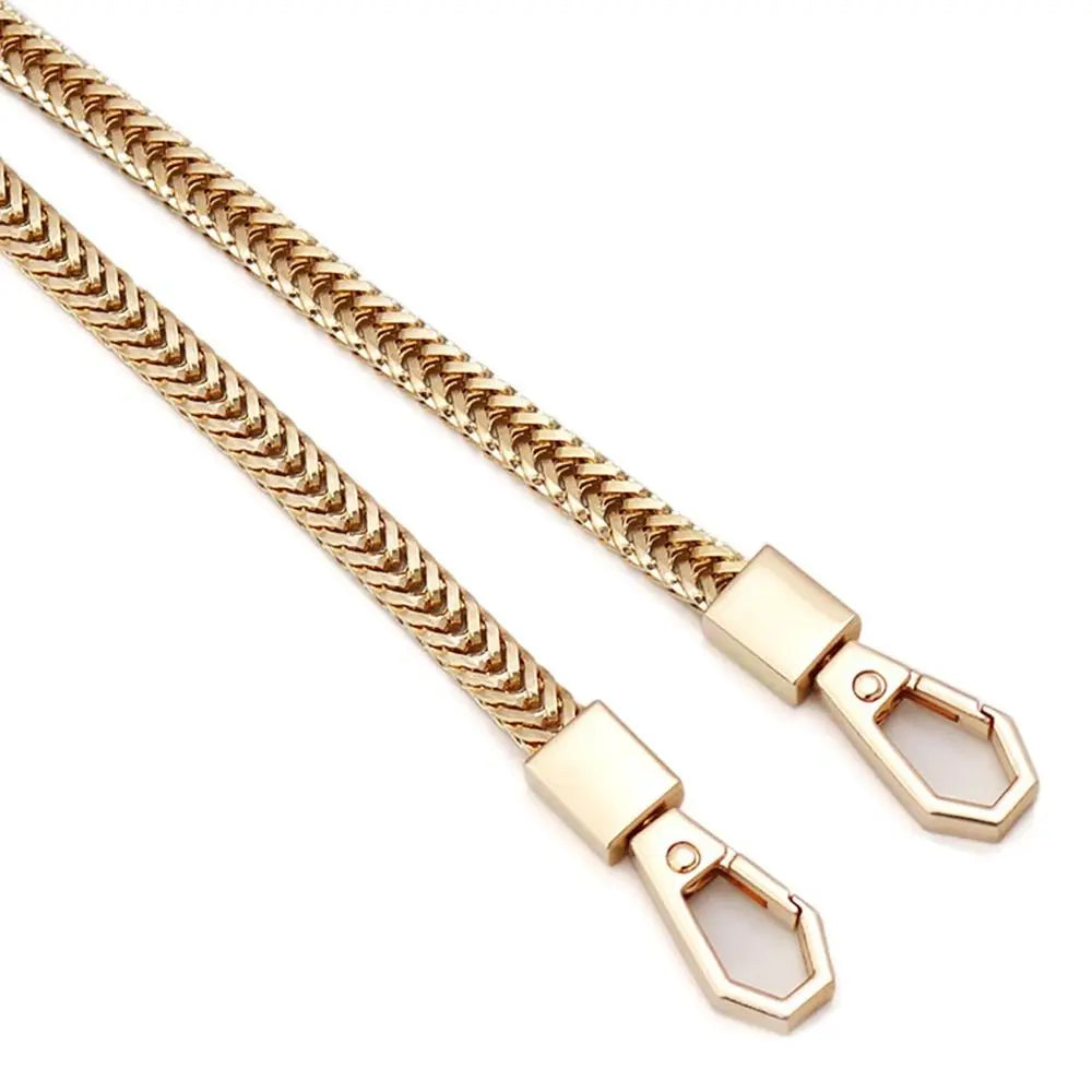 A close-up of a gold-toned metal bag chain strap with a textured link design.