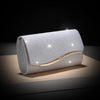 Silver sequined envelope clutch with a gold chain resting on a wooden surface.
