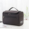 A dark gray portable Oxford cloth toiletry bag lying on a white surface.