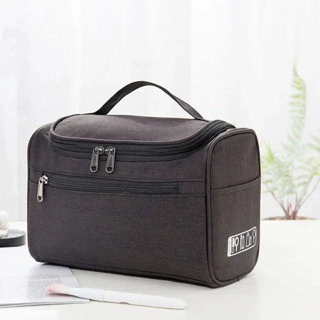 A dark gray portable Oxford cloth toiletry bag lying on a white surface.