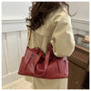 A close-up of a reddish-brown leather shoulder tote bag carried by a person wearing a cream-colored jacket.