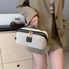 A beige travel toiletry bag with black trim and gold hardware is held by a person wearing a tan blazer.
