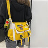 A yellow and white nylon crossbody shoulder bag with green charm and black fabric worn by a person.