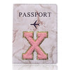 Funda de pasaporte de imitación de cuero rosa con una X grabada en oro y un diseño de avión negro.