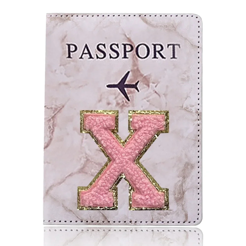 Funda de pasaporte de imitación de cuero rosa con una X grabada en oro y un diseño de avión negro.
