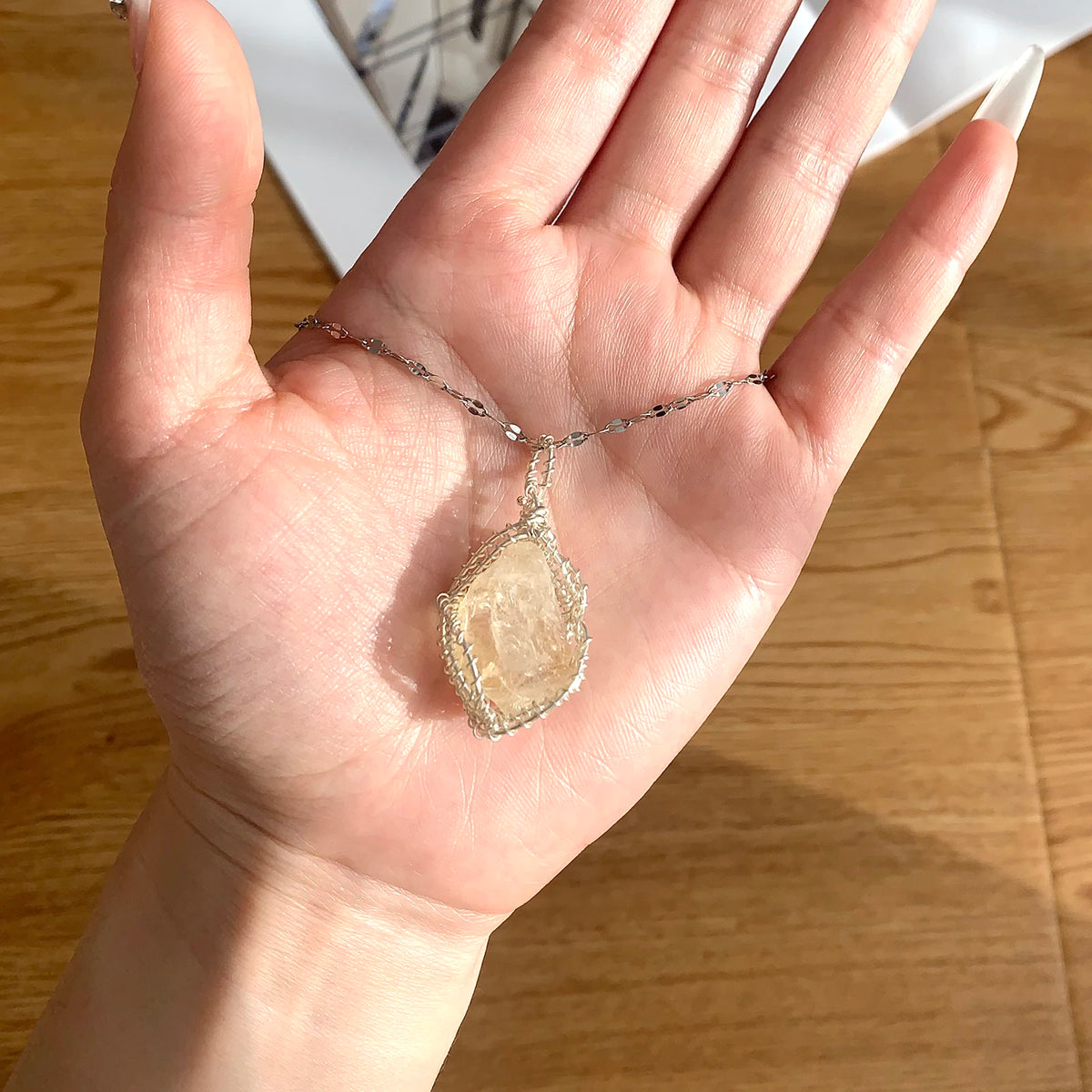 A hand holds a handcrafted amethyst crystal pendant necklace featuring a light yellow stone wrapped with copper wire.