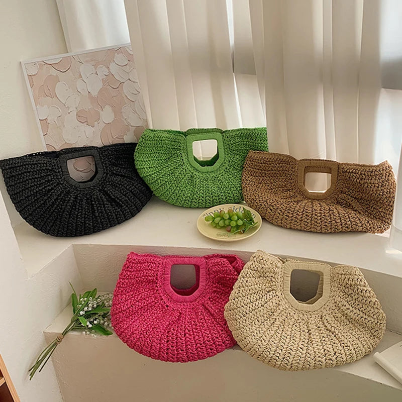 A collection of woven rattan half-moon beach handbags in various shades of green, brown, and pink displayed on a white shelf.