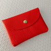 A vibrant red genuine leather card holder with a gold-toned clasp resting on a white textured surface.