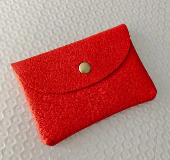 A vibrant red genuine leather card holder with a gold-toned clasp resting on a white textured surface.