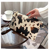 A hand holds a leopard print PU leather wrist bag with gold hardware on a wooden surface.