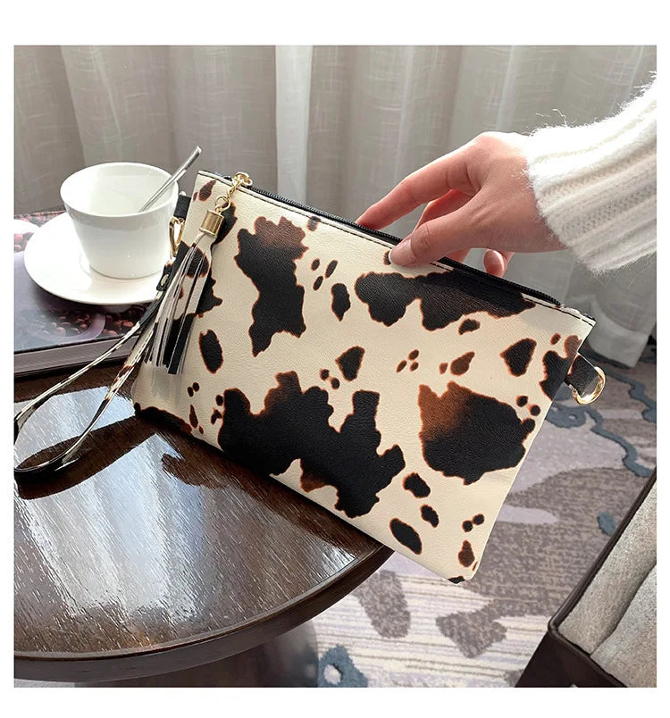 A hand holds a leopard print PU leather wrist bag with gold hardware on a wooden surface.