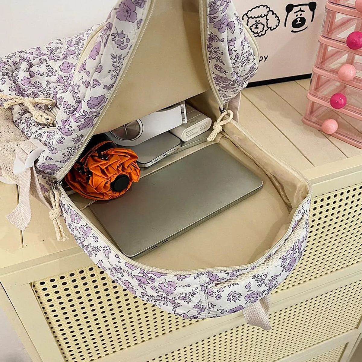 A purple and white floral quilted backpack set with a laptop inside, resting on a light wood surface.