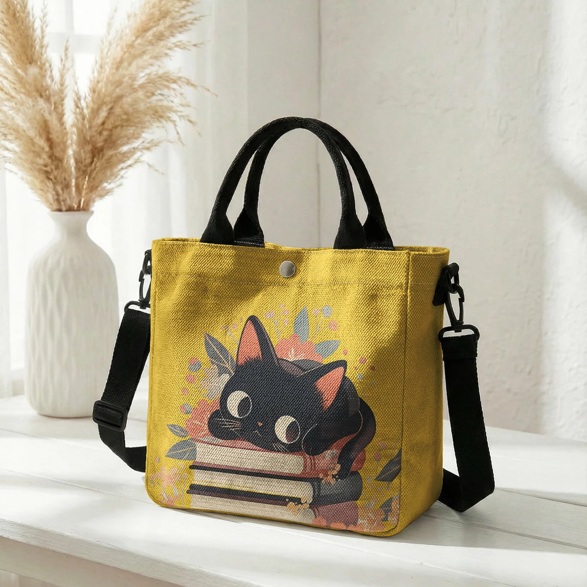 Gelige Tasche mit Blumen-Katzenmuster und schwarzem Riemen auf weißem Untergrund.