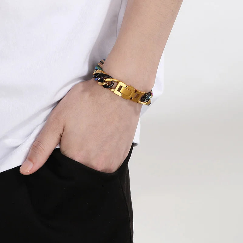 A close-up of a gold and blue chunky Cuban link bracelet worn on a wrist against a white shirt.