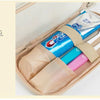 A beige travel bag is shown open, containing various toiletries and a blue cream tube.