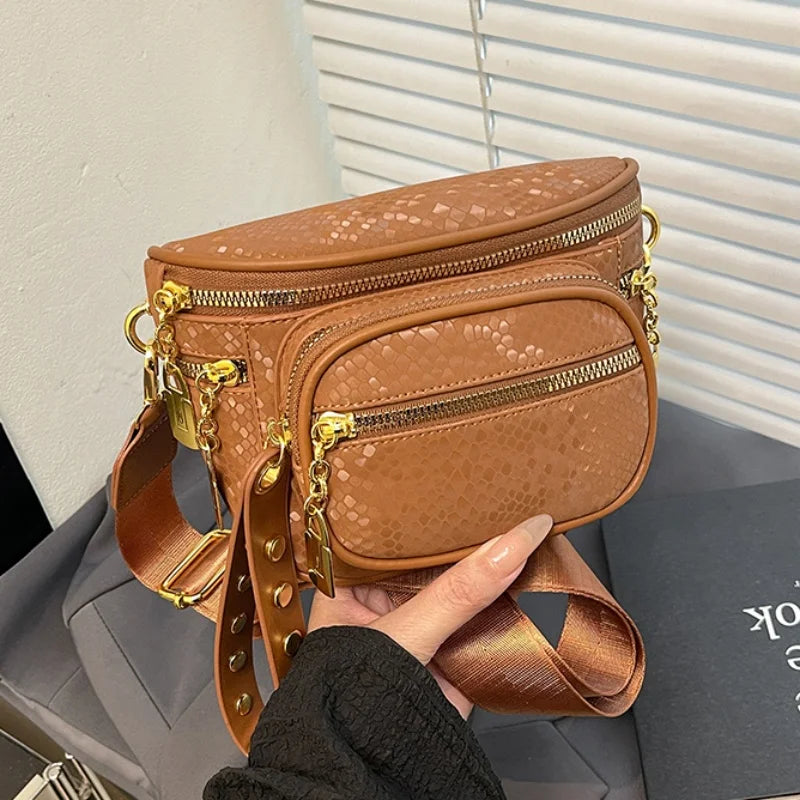A brown women's rivet waist bag crossbody fanny pack with gold hardware being held by a hand.