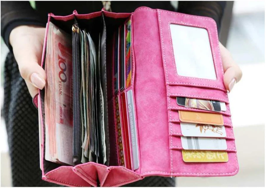 A pink clutch wallet with multiple slots and an ID window is held in a person's hand.