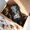 Cartera de cuero sintético negro con cierre de cremallera y diseño bordado de vaca blanca, dentro de una caja de cartón