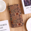 A patterned leather wallet with multiple card slots rests on a wooden surface next to a white bowl and a book.