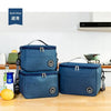 Two dark blue insulated portable lunch bags with shoulder straps resting on a wooden surface.