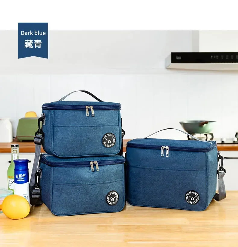 Two dark blue insulated portable lunch bags with shoulder straps resting on a wooden surface.