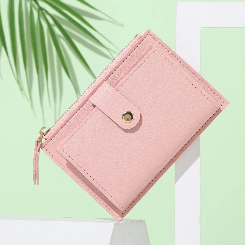 A pink leather compact wallet with a flap closure and zipper is displayed against a light green background.