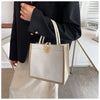 A person holds a beige floral linen tote bag with woven handles and a wooden closure against a white background.