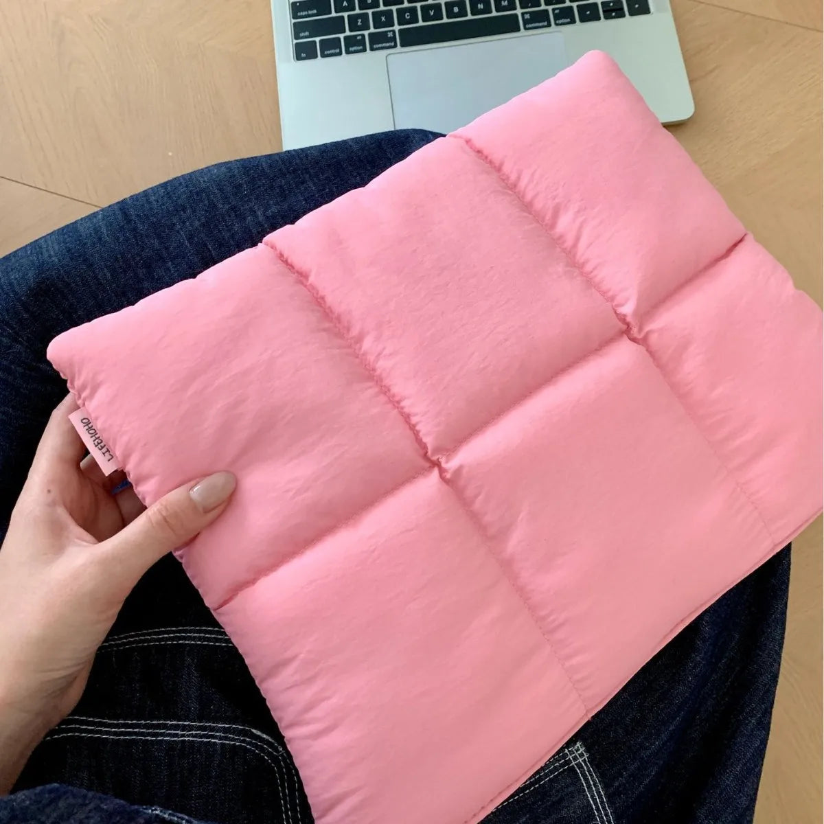 A pink quilted laptop sleeve is being held by a hand, resting on a dark blue denim fabric.