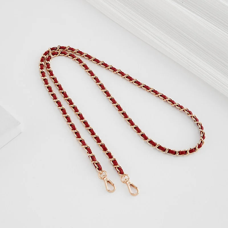 A close-up of a red beaded strap with gold-toned buckles laid diagonally on a white surface.