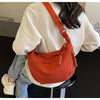 A woman is wearing an orange canvas crossbody shoulder bag over a white jacket while sitting.
