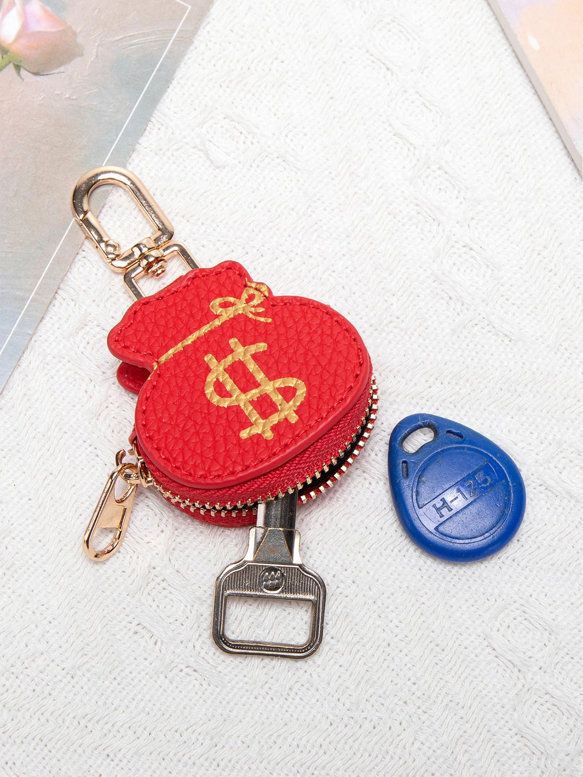 Cartera de monedas roja con diseño de signo de dólar dorado en llavero metálico y etiqueta de seguridad azul.