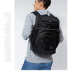 A man wearing a grey sweater and jeans is holding a black insulated travel cooler backpack.