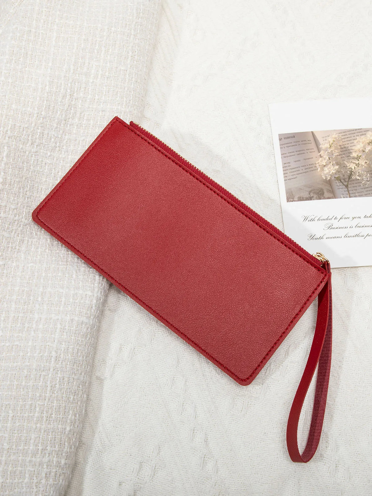 A red PU leather coin purse and card holder with a thin strap resting on a white textured fabric.