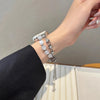 Nahaufnahme einer Hand mit einem verstellbaren Metallarmband aus klaren Kristallperlen vor hellem Hintergrund.