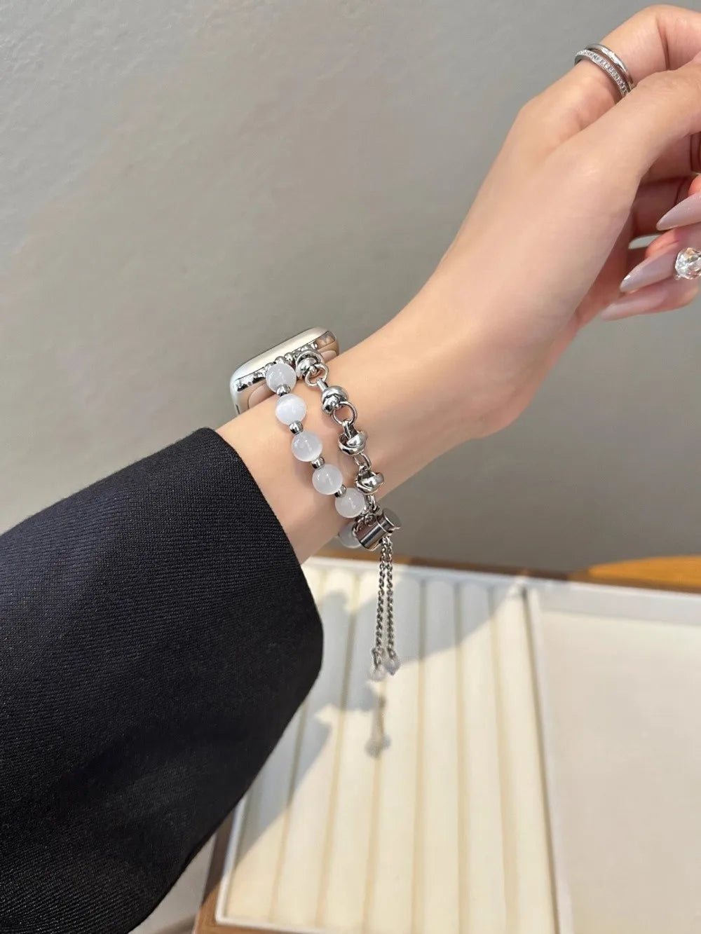 Nahaufnahme einer Hand mit einem verstellbaren Metallarmband aus klaren Kristallperlen vor hellem Hintergrund.