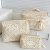 A set of three floral print quilted cosmetic bags in cream and beige tones displayed on a white surface.