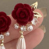 Gold and pearl ear studs featuring a deep red velvet rose design on a finger.
