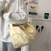 A beige canvas crossbody travel tote bag is shown being held by a person, next to some packaged goods.