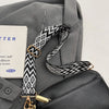 A gray jacket features a black and white geometric patterned strap attached to a leather crossbody bag.